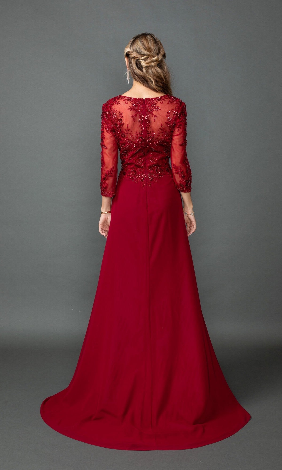 A woman stands with her back to the camera in a floor-length Dancing Queen 4543 gown featuring a sequin lace bodice and sheer embroidered long sleeves, set against a plain gray background.